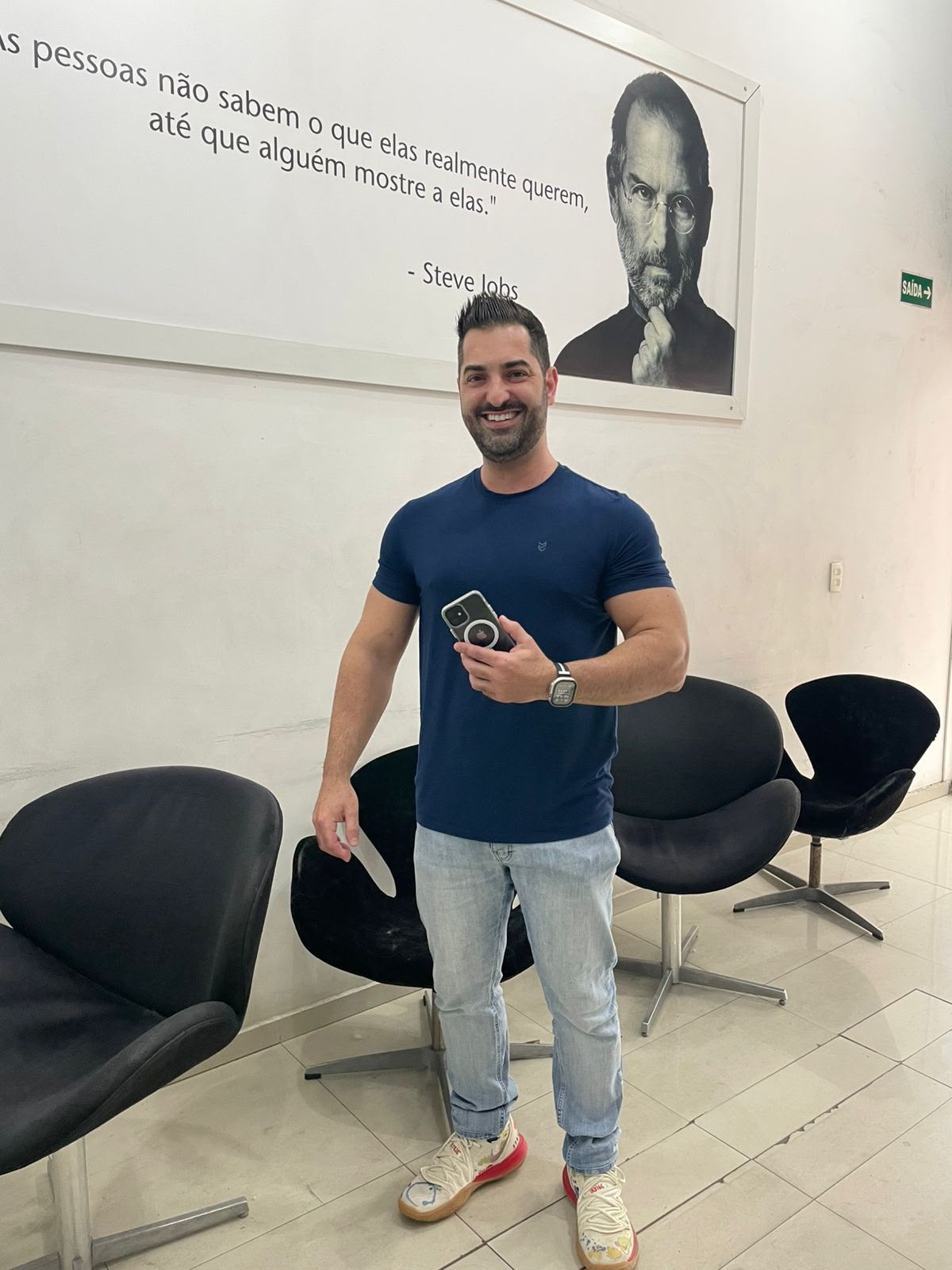 Cliente de camiseta azul com o celular e o carregador MagSafe na iPlanet